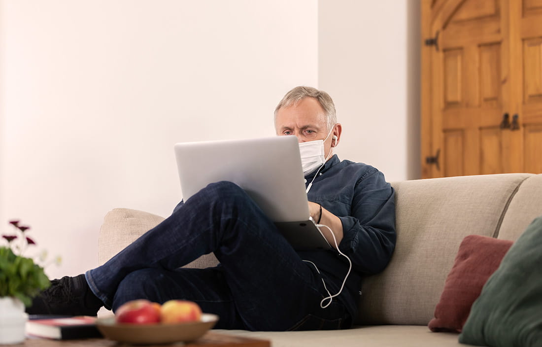 Man sitting on the couch wearing a mask on his laptop