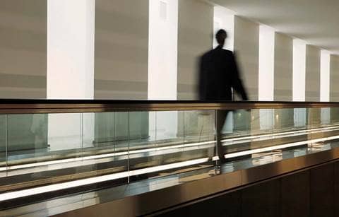 Picture of a blurry man walking down a corridor with glass railing to his right.