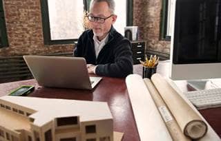 Middle-aged man with glasses looking at his laptop computer screen.