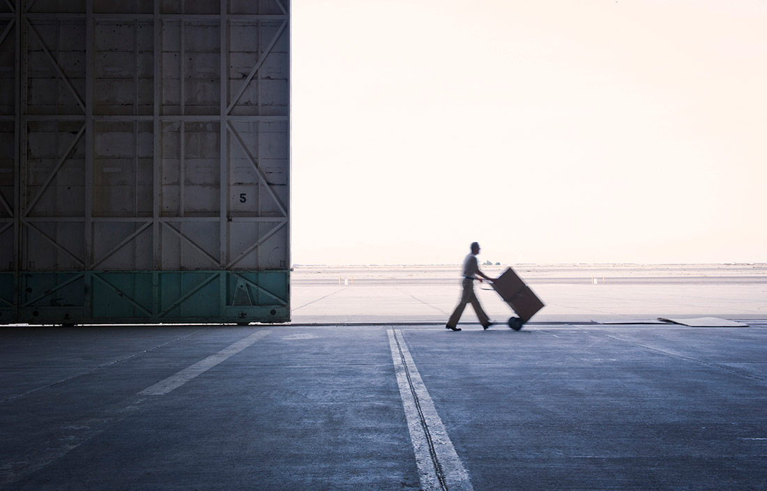Man pushing a box of supplies on a push cart near an airport hangar door.