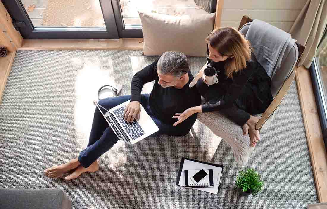 Woman sitting in chair drinking coffee and a man sitting on the floor using his laptop computer.