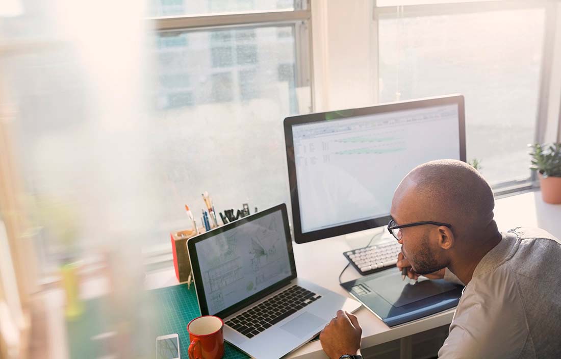 Man sitting at a desk with a laptop and desktop computer