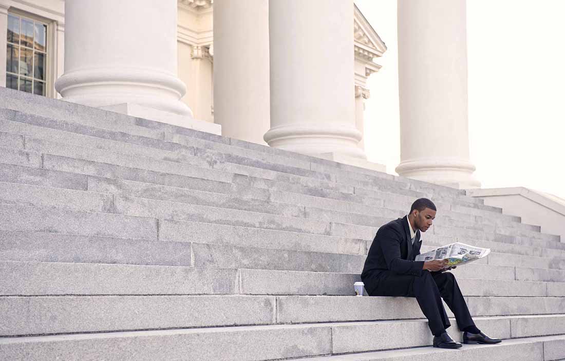 Man sitting on outside stairs reading a newspaper