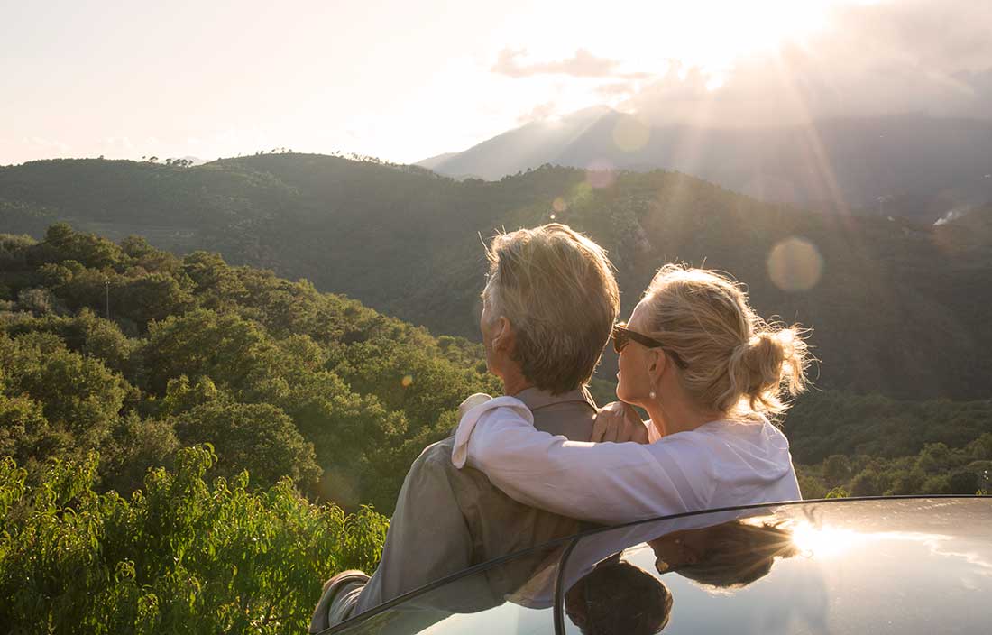 Man and woman sitting on the back of a car looking out at mountains