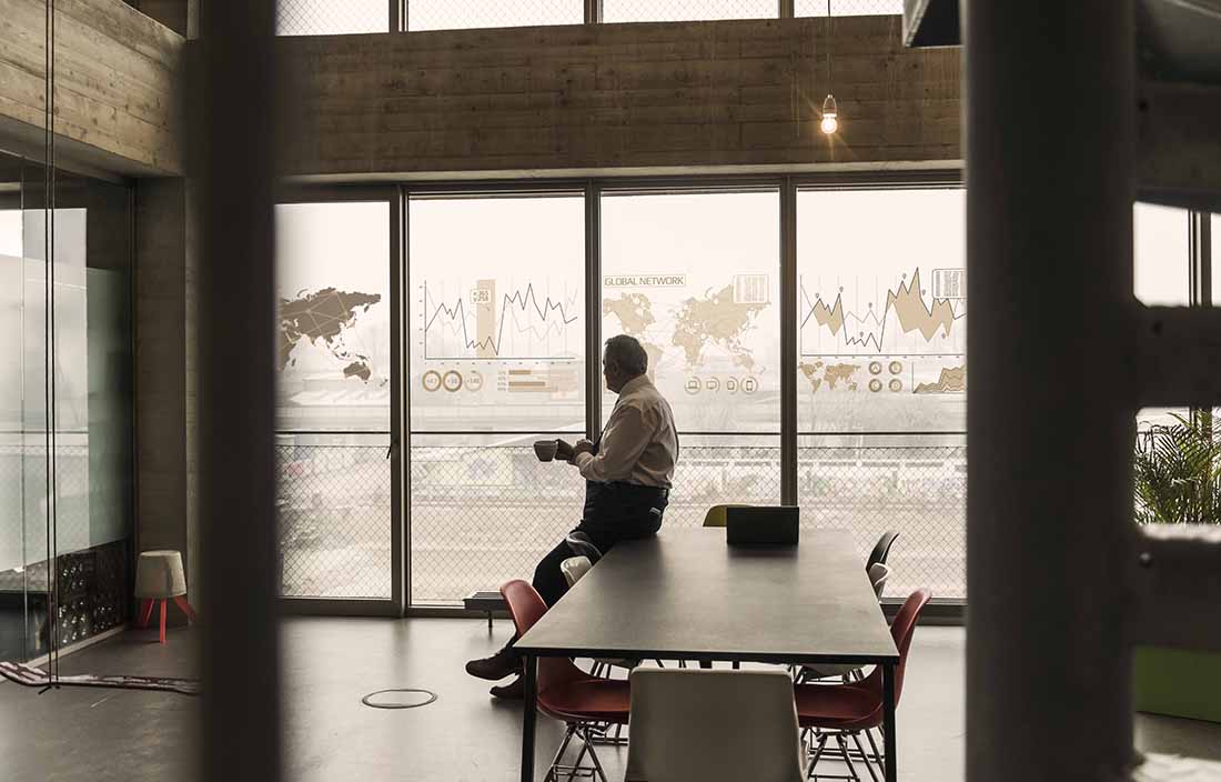 Middle-aged business man leaning and sitting against a table while holding a cup of coffee.