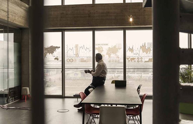 Middle-aged business man leaning and sitting against a table while holding a cup of coffee.