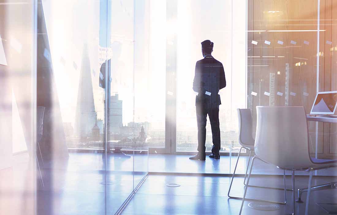 Younger businessman standing in the corner of the office looking out the window.