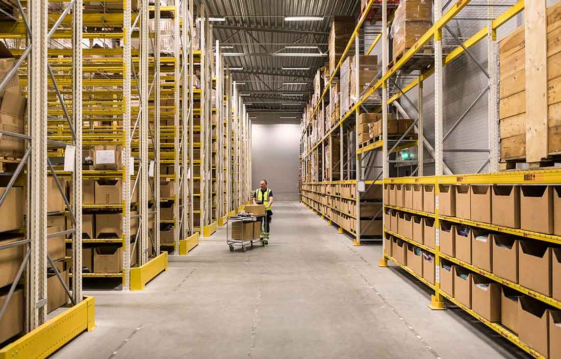 Factory worker loading supplies into cart from warehouse shelves.