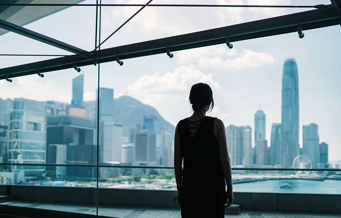 A woman standing looking over a bridge into a city bay view.