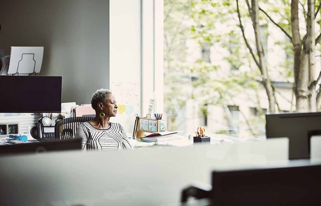 Elderly woman sitting in her home office looking out the window.