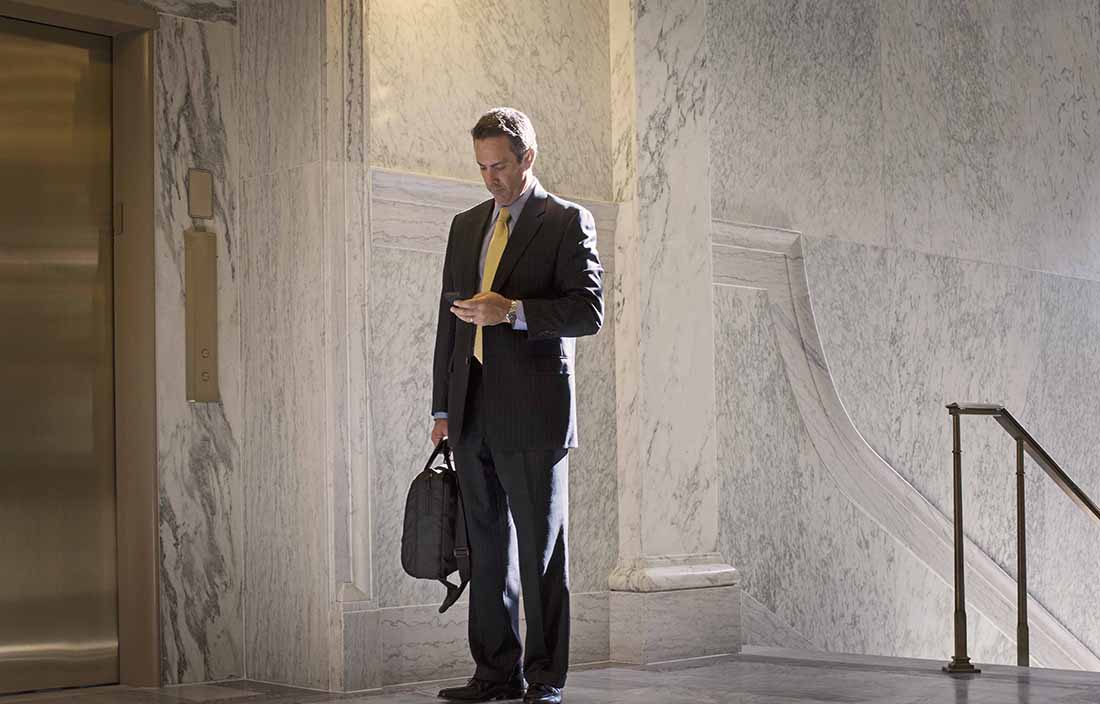 Businessman standing at the top of a staircase looking down and checking his cell phone.