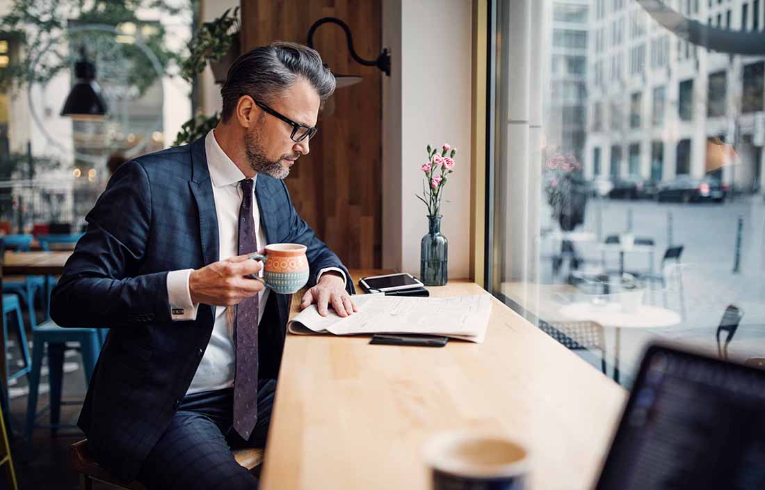 Man sitting in a coffee shop window, reading the paper and drinking coffee