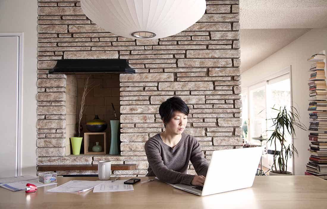 Woman sitting at kitchen table using laptop computer for work.