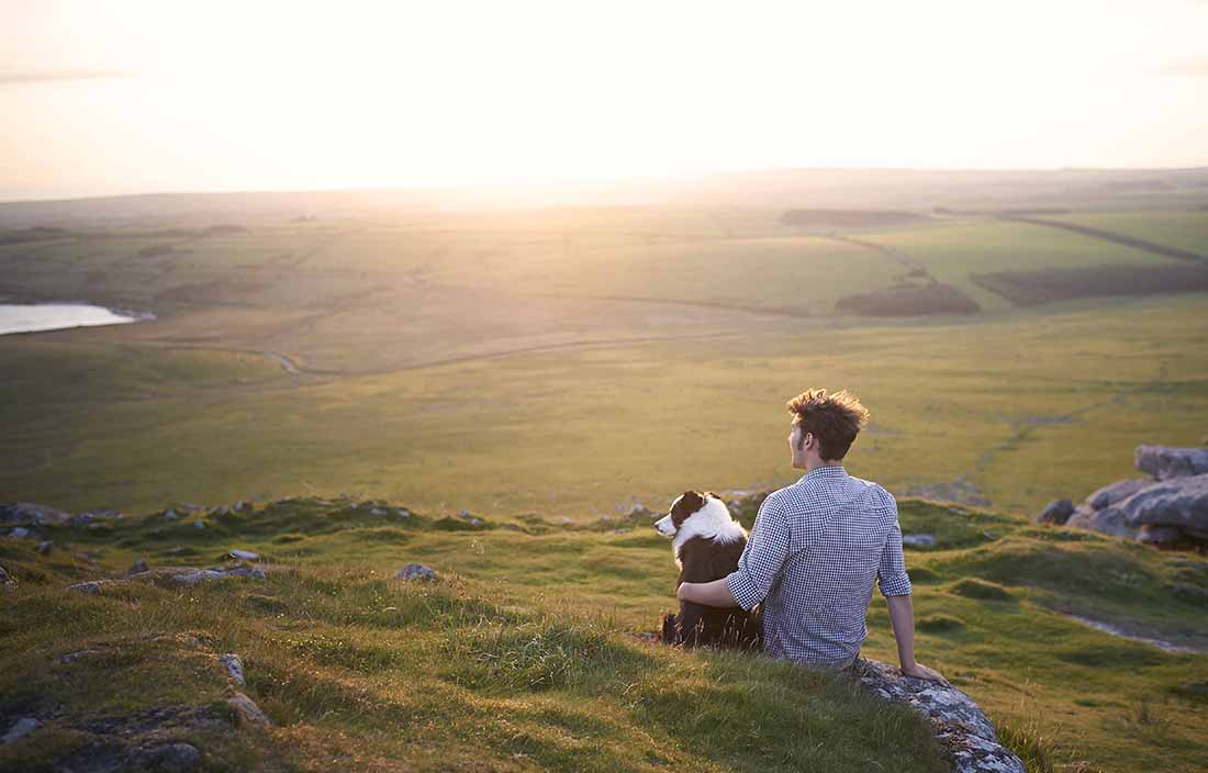 A man sitting on a grassy hill with his dog