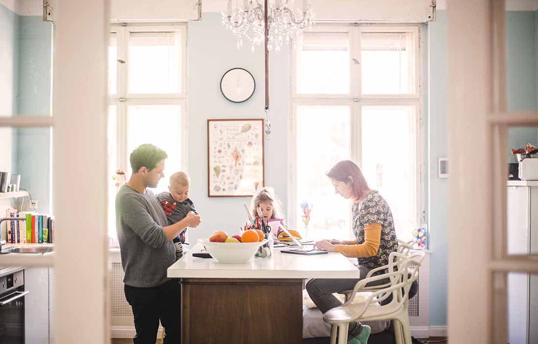 Young coupe working from home in their kitchen with their toddler kids nearby.