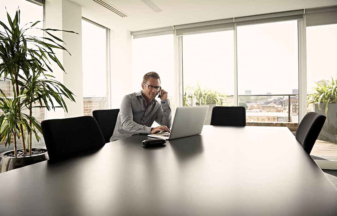 Business man sitting at a conference room table using his laptop computer and cell phone.