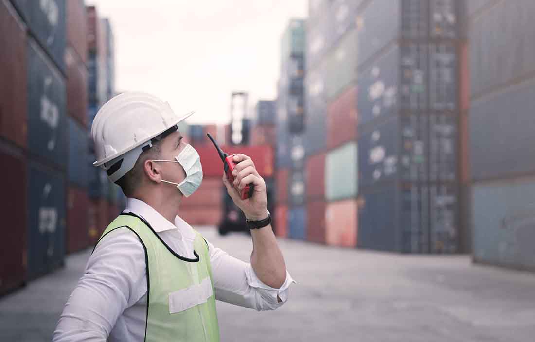 Worker in a hard hat, wearing a mask, talking into a walkie talkie