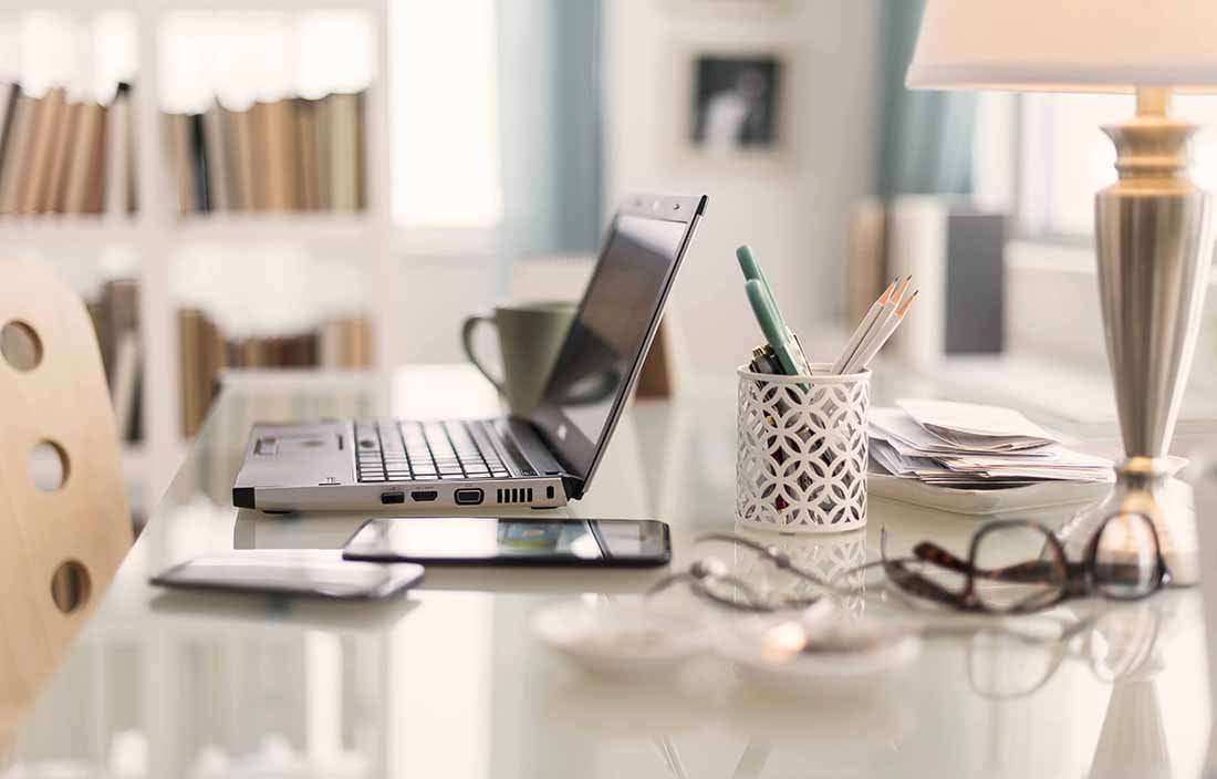 Close-up view of a desk at home with a laptop computer and various other office supplies.