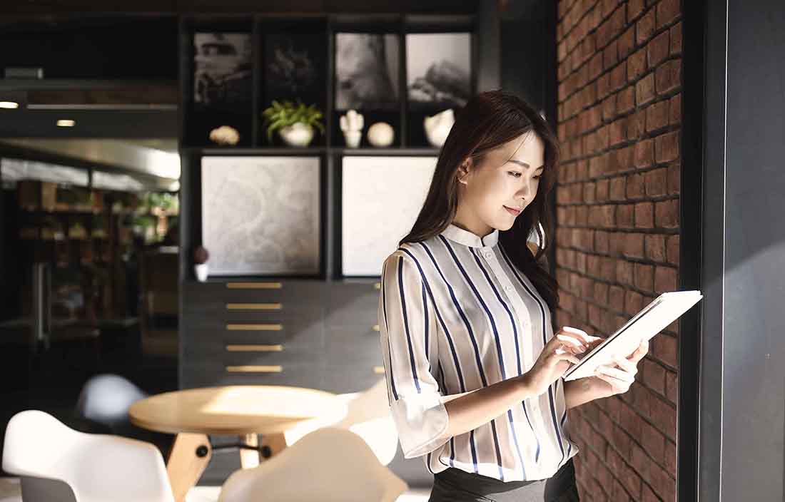 Woman standing by a brick wall on a tablet