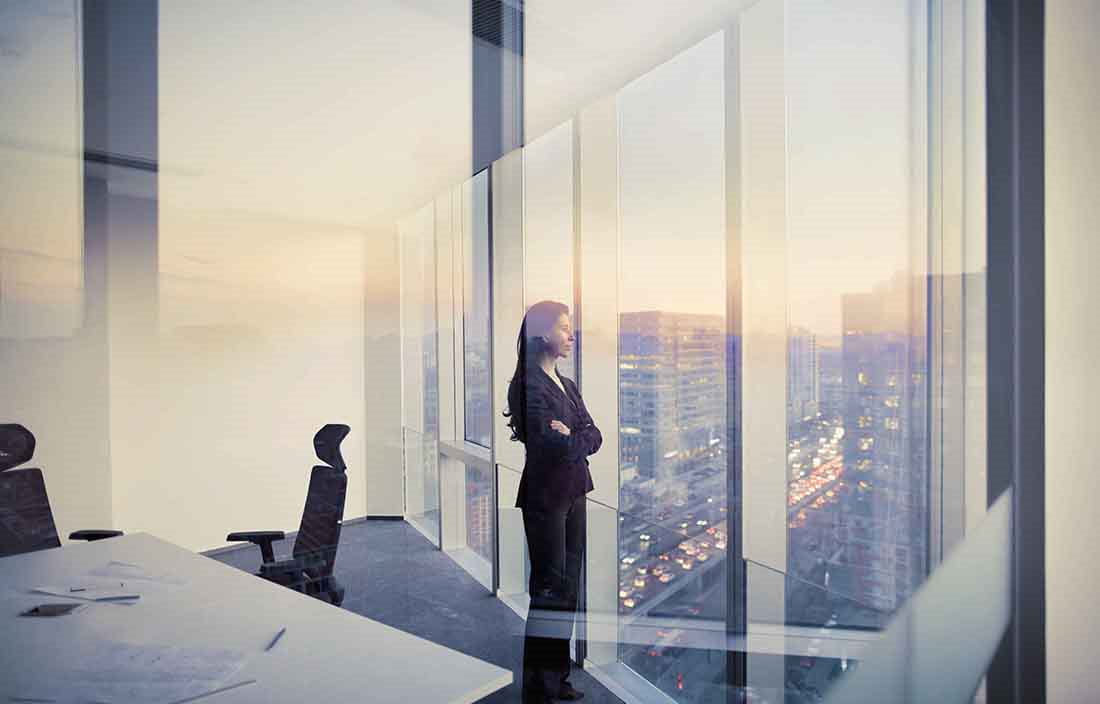 Woman standing in office looking out the window at the city skyline.