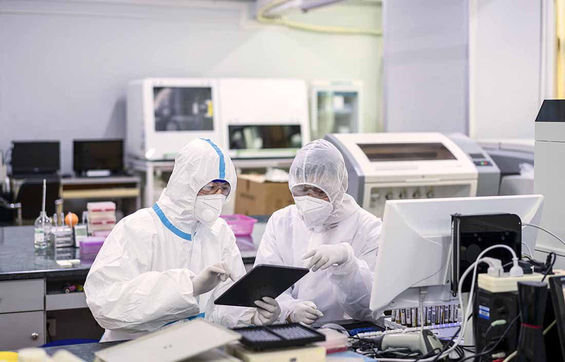 Two lab workers in PPE equipment reviewing information on a handheld device.