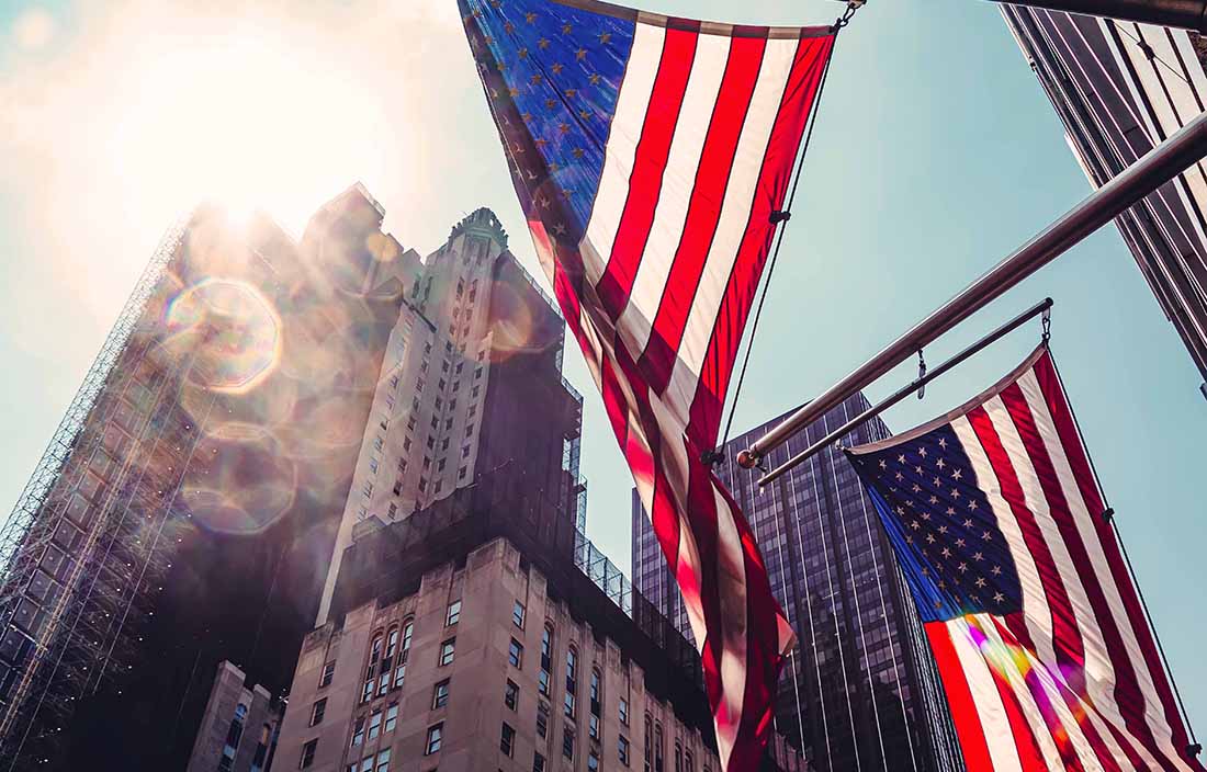 Two american flags flying in the air by a building