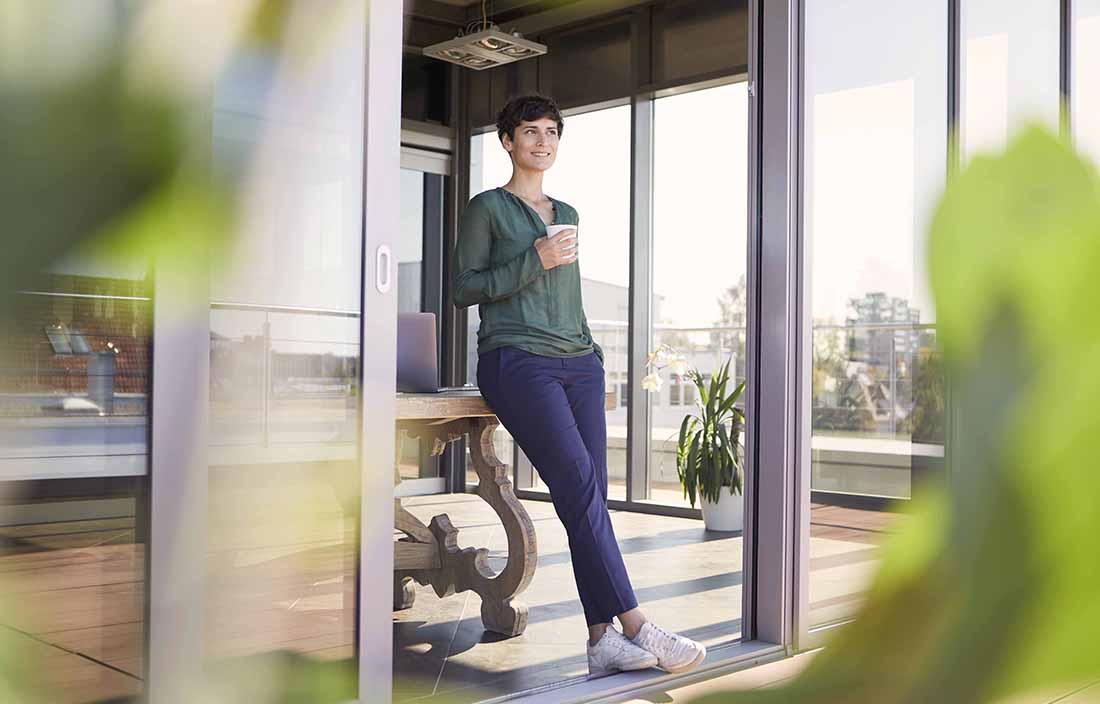 Woman leaning against a sliding glass door, drinking coffee