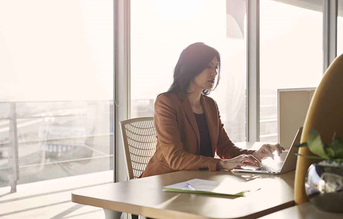 Businesswoman working in an office during the day with glass windows behind her.