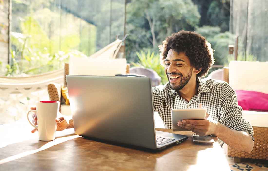 Man working from home smiling and laughing while using a laptop computer.
