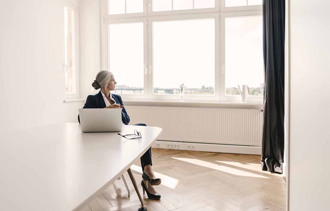 Woman sitting at a table on her laptop, looking out the window