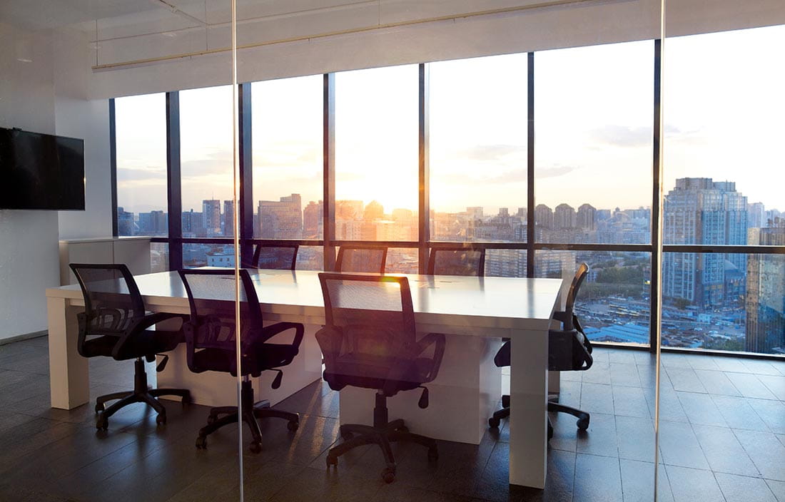 View of an empty conference room with a sunset in the distance through the office windows.