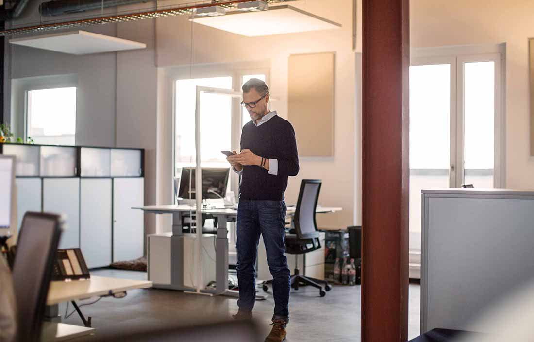 Businessman in casual clothes standing in the office checking his cellphone.