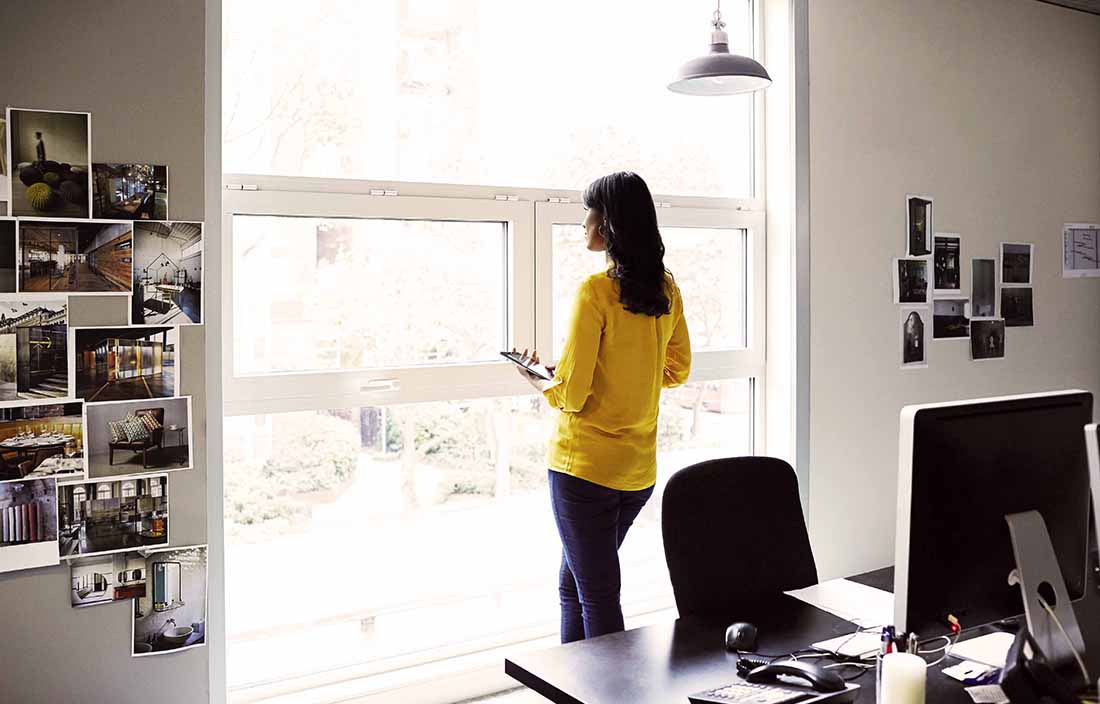 Woman looking out a window holding a tablet