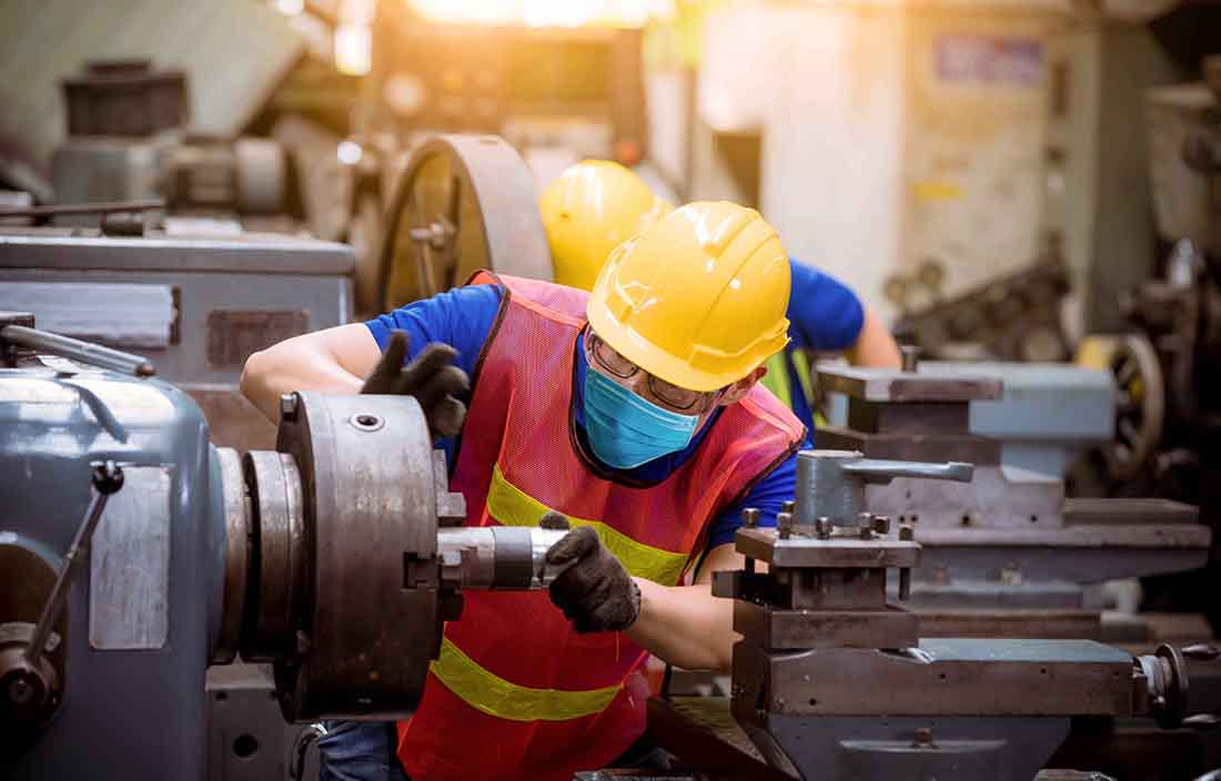 Automotive worker using a machine while wearing a hard hat.