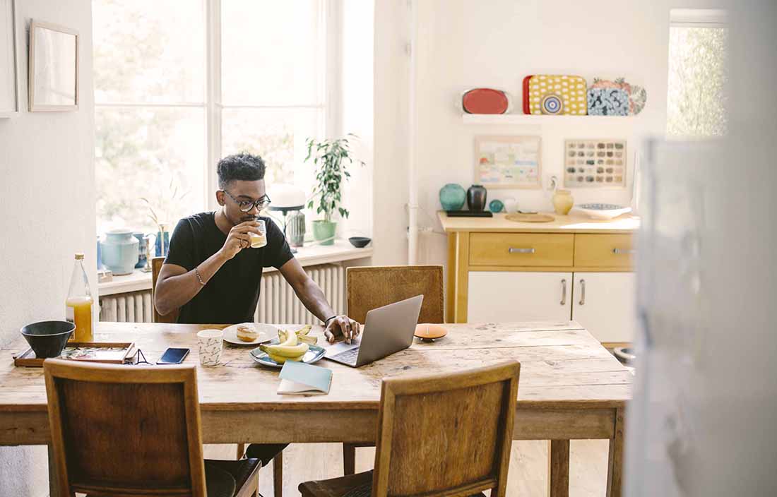 Guy working from home on a laptop computer at the kitchen.