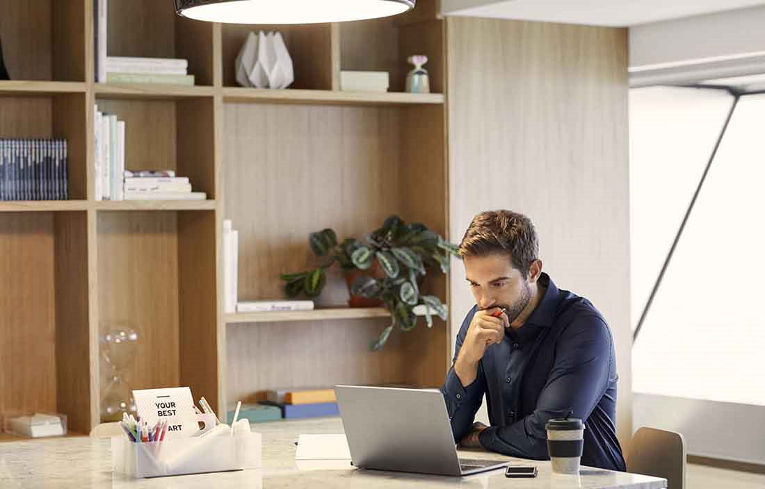 Businessman working from his home office in casual clothes looking at a laptop computer.