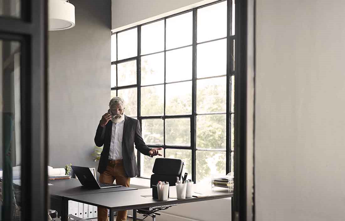 Businessman working at home office standing by his desk taking a phone call.