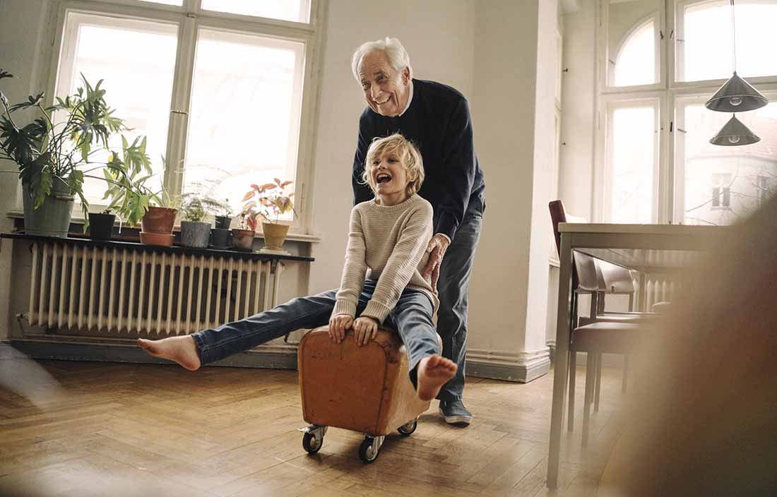 Elderly man playing with a kid in a living room.