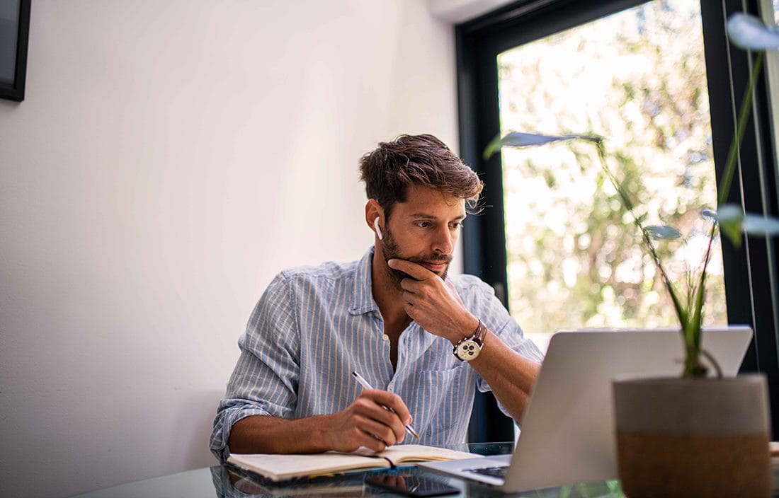 Businessman working in his home office using a laptop computer with a notepad in front of him.