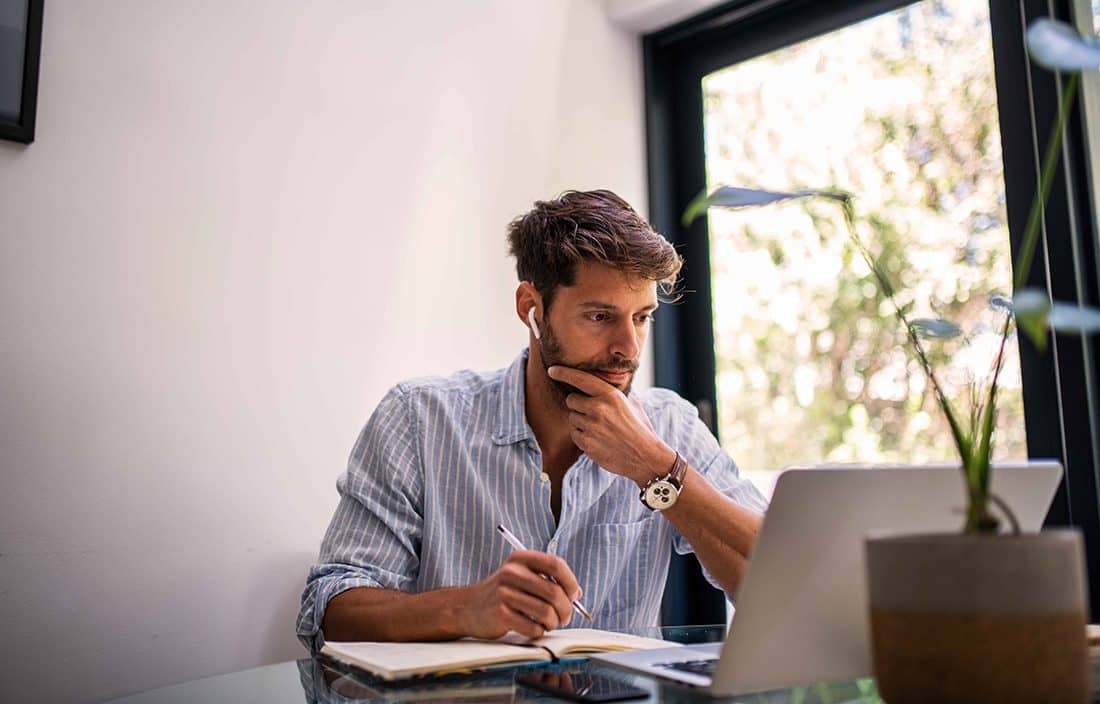 Businessman working in his home office using a laptop computer with a notepad in front of him.