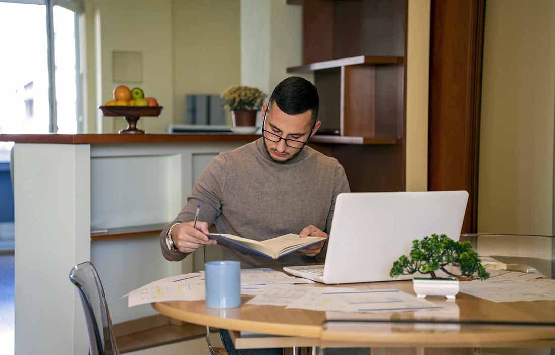 Man wearing glasses reading a book at a table.