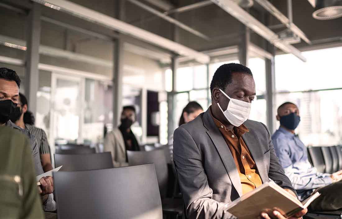 A group of business people in a waiting area wearing protective face masks for COVID-19.