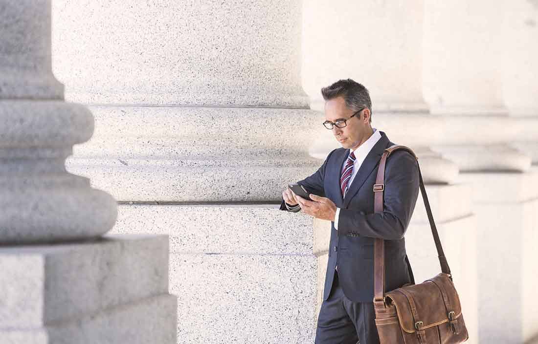 Businessman checking cell phone standing next to pillars of a government building.