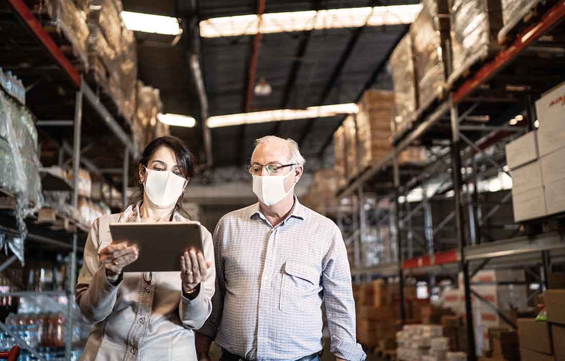 Two businesspeople walking through a warehouse reviewing levels of supply.