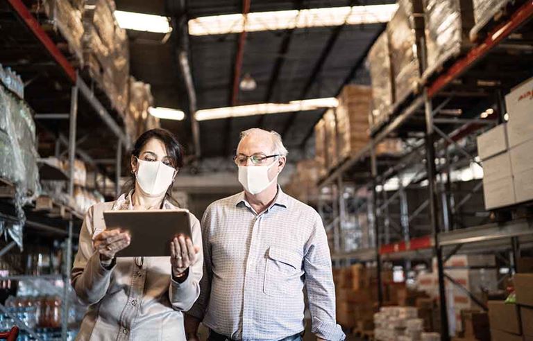 Two businesspeople walking through a warehouse reviewing levels of supply.