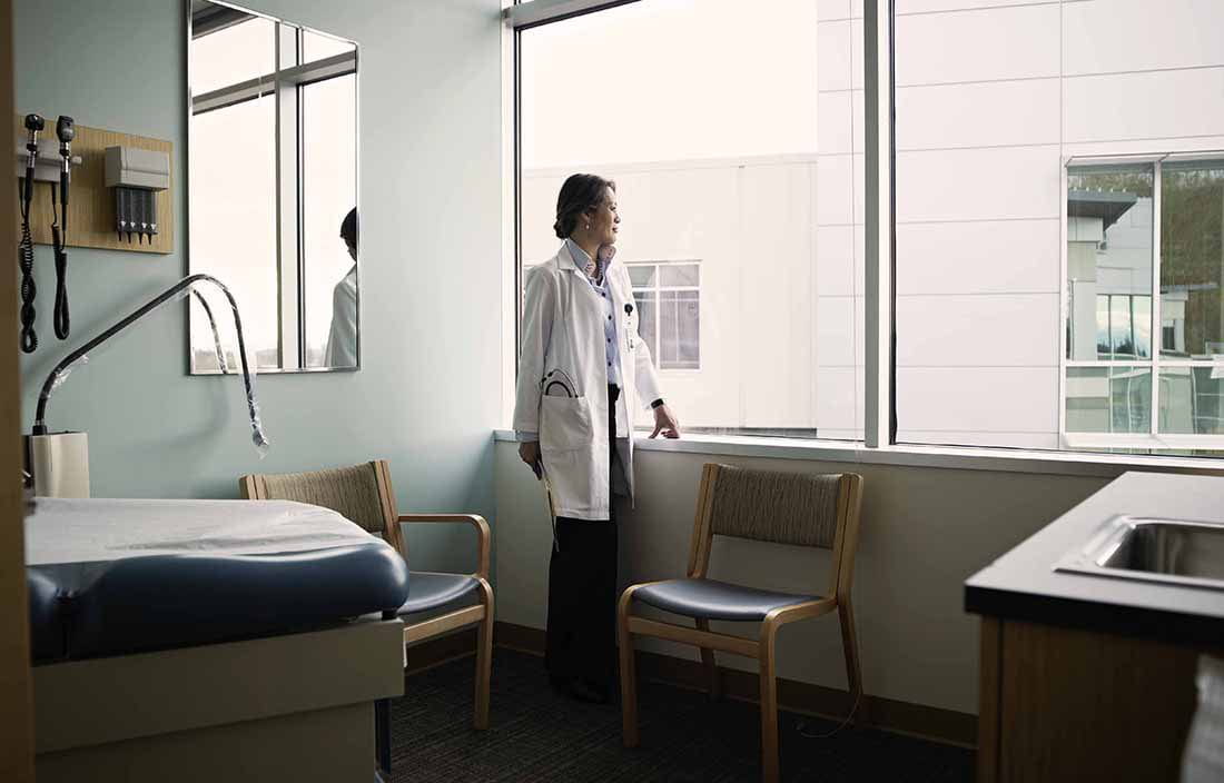 Doctor standing in the corner of a patient room looking out the window.
