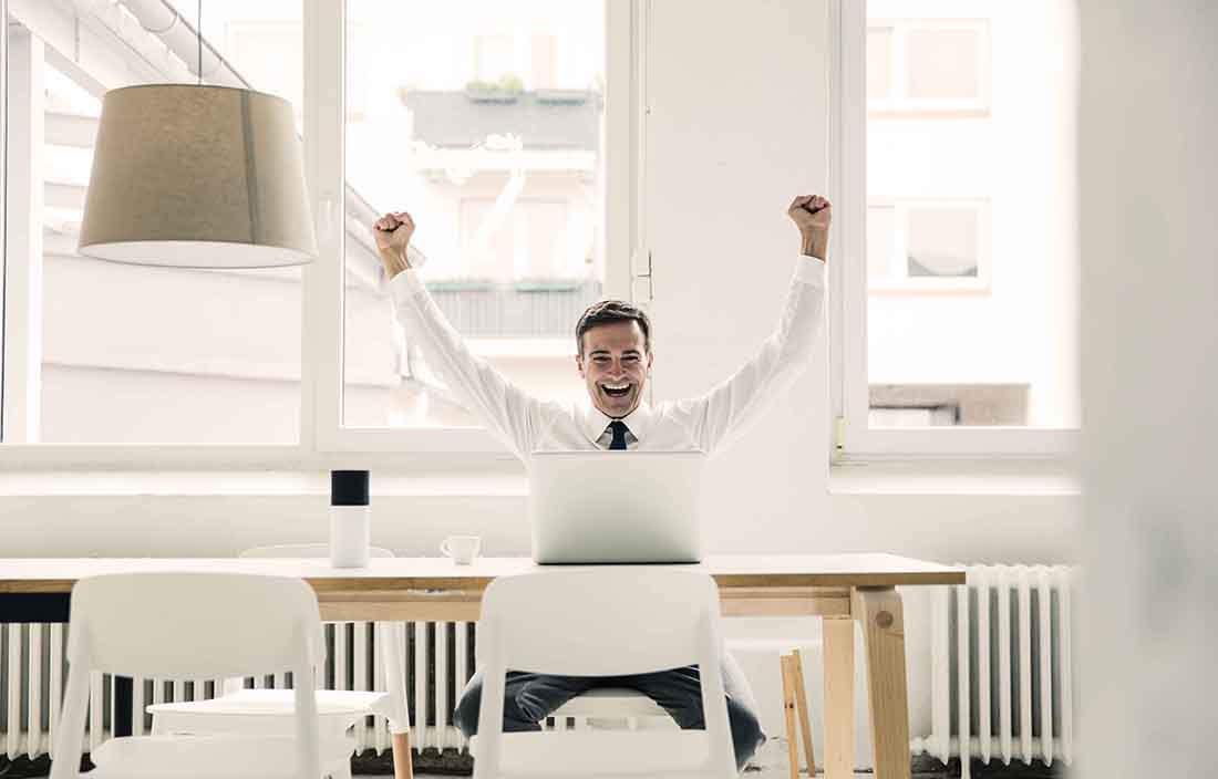 Businessman celebrating at his desk with his hands in the air.
