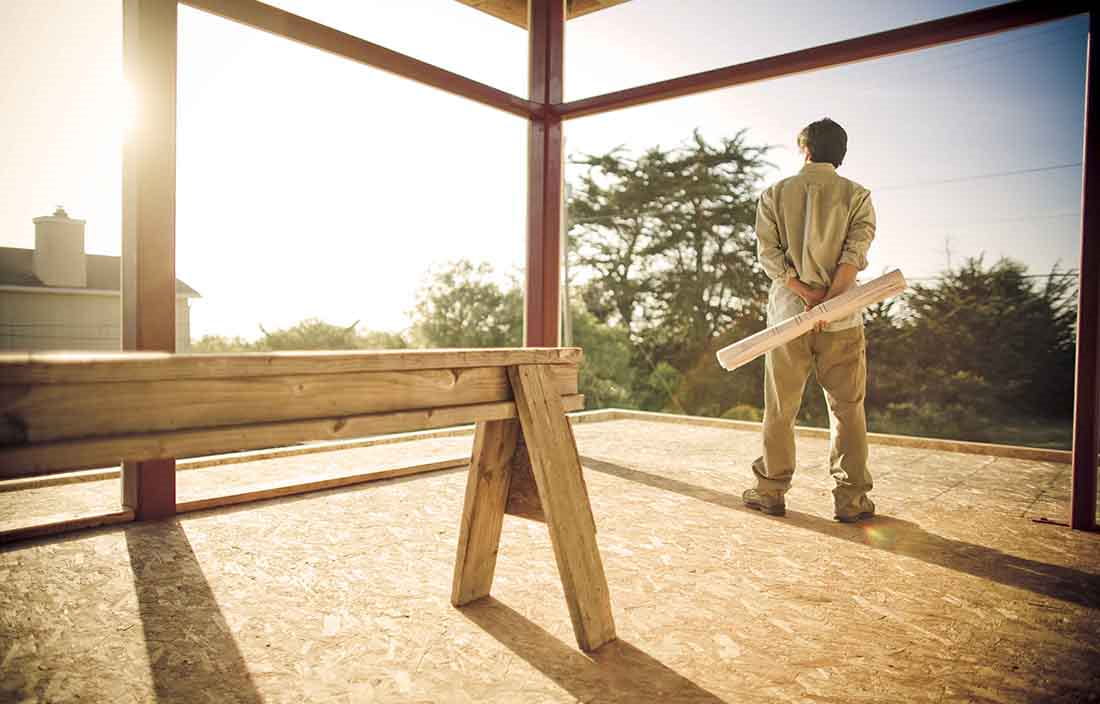 Construction worker holding a piece of wood while looking at the frame of a building.