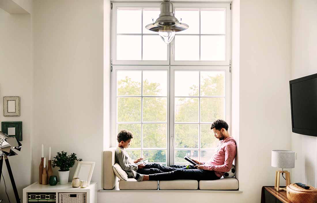 A father and son sitting in a window sill using tablet devices.