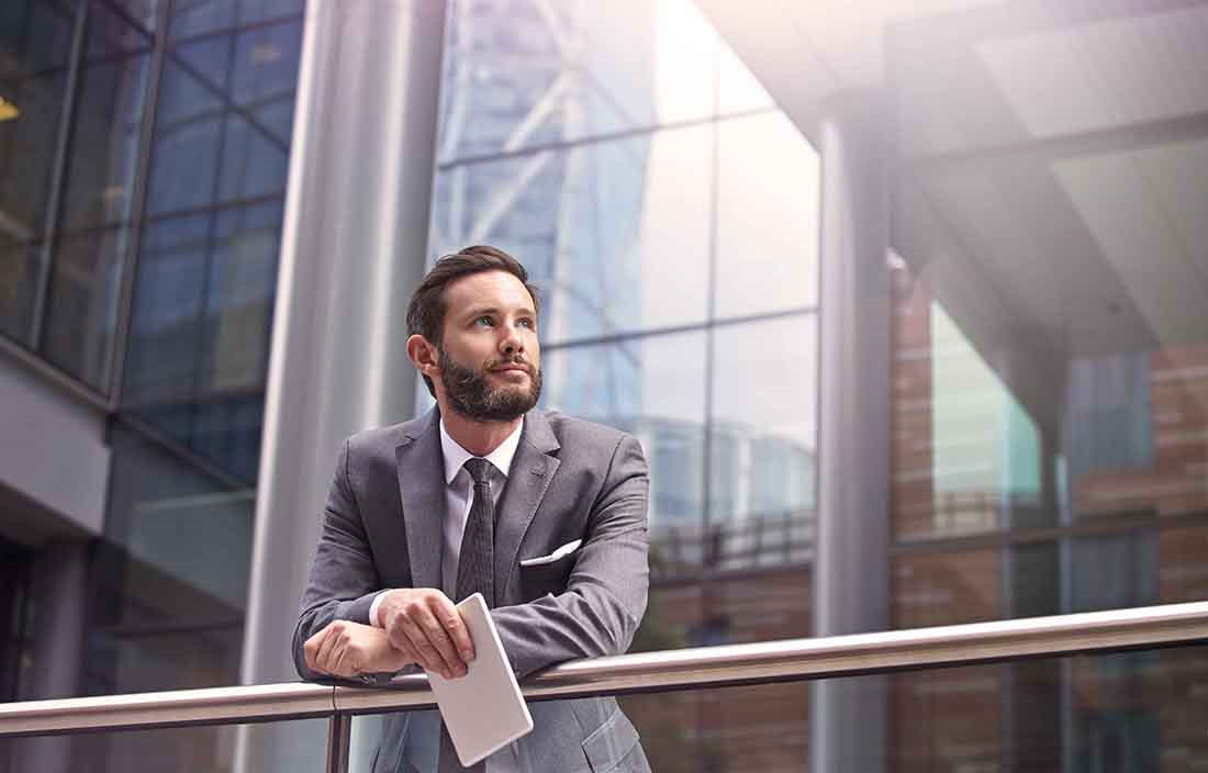 A businessman leaning against a metal railing outside a building.